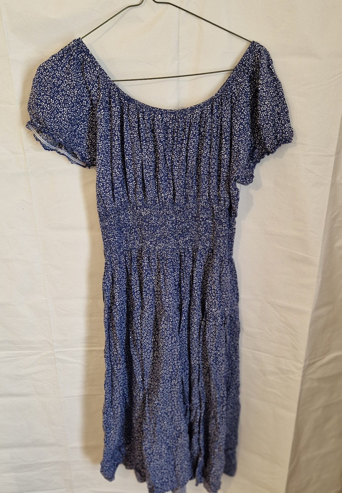 A blue knee-length dress with a white floral pattern, short sleeves, and a smocked waist.