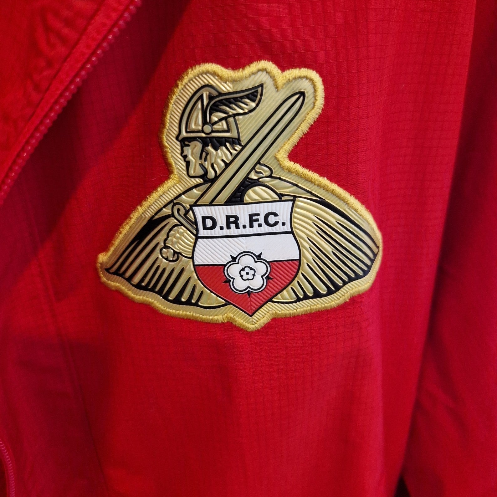A red Doncaster Rovers training jacket featuring a detailed embroidered club crest on the chest.
