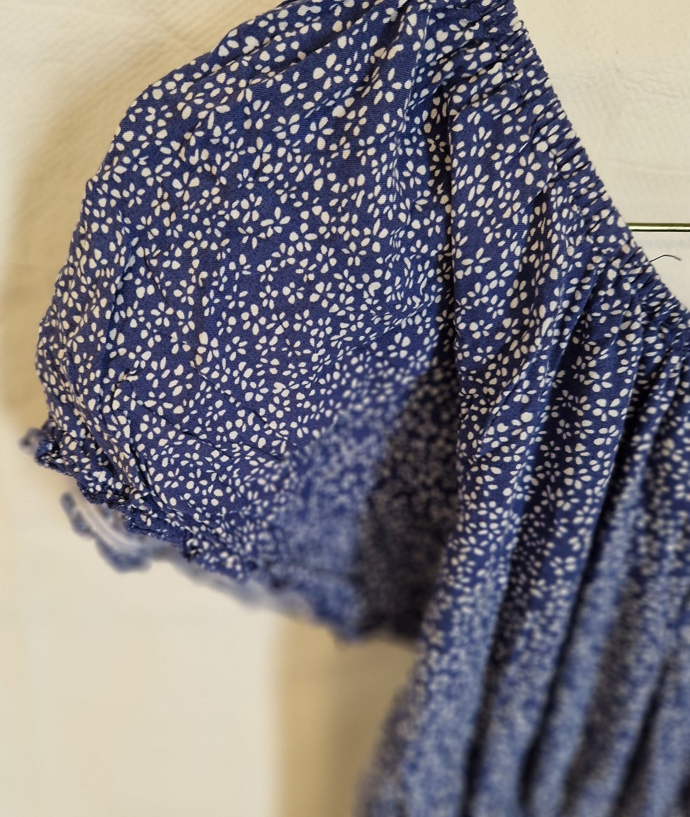 A close-up of a blue knee-length dress featuring a white floral pattern and gathered short sleeves.