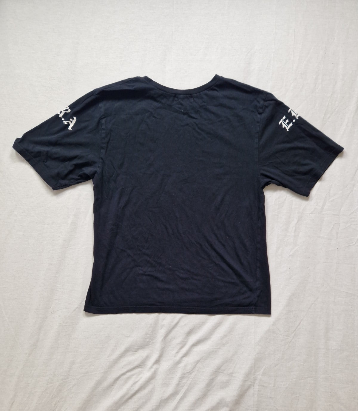 Black t-shirt with white text on sleeves laid flat on a white surface