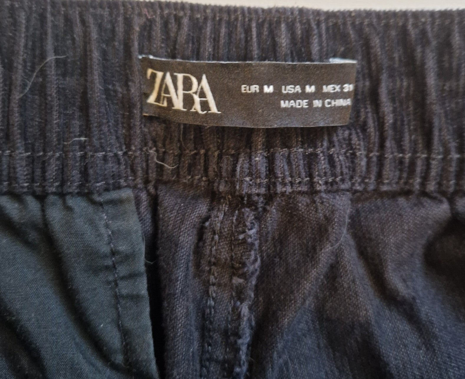 Close-up of the black Zara label on the elastic waistband of men's cargo jogger pants.