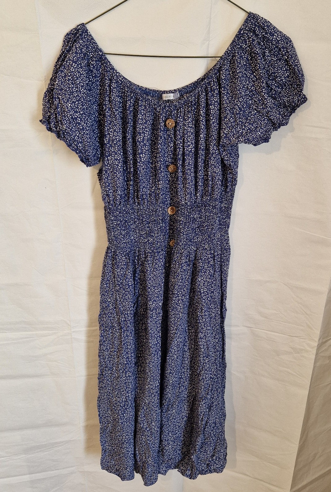 A blue knee-length dress with a white floral pattern, short puff sleeves, and button accents.