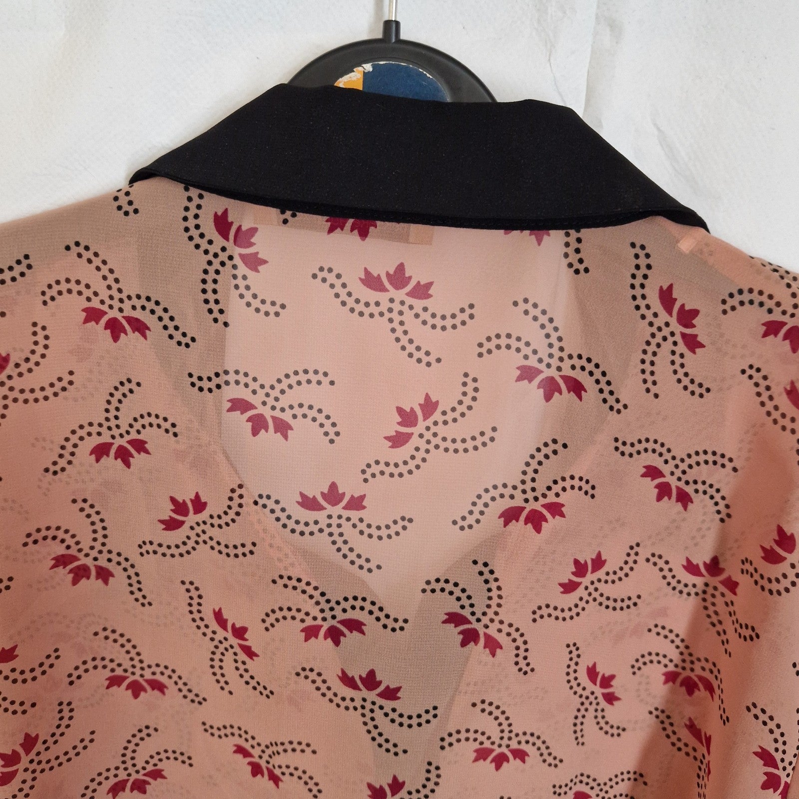 A peach-colored chiffon blouse featuring a black dotted floral pattern and a black collar.
