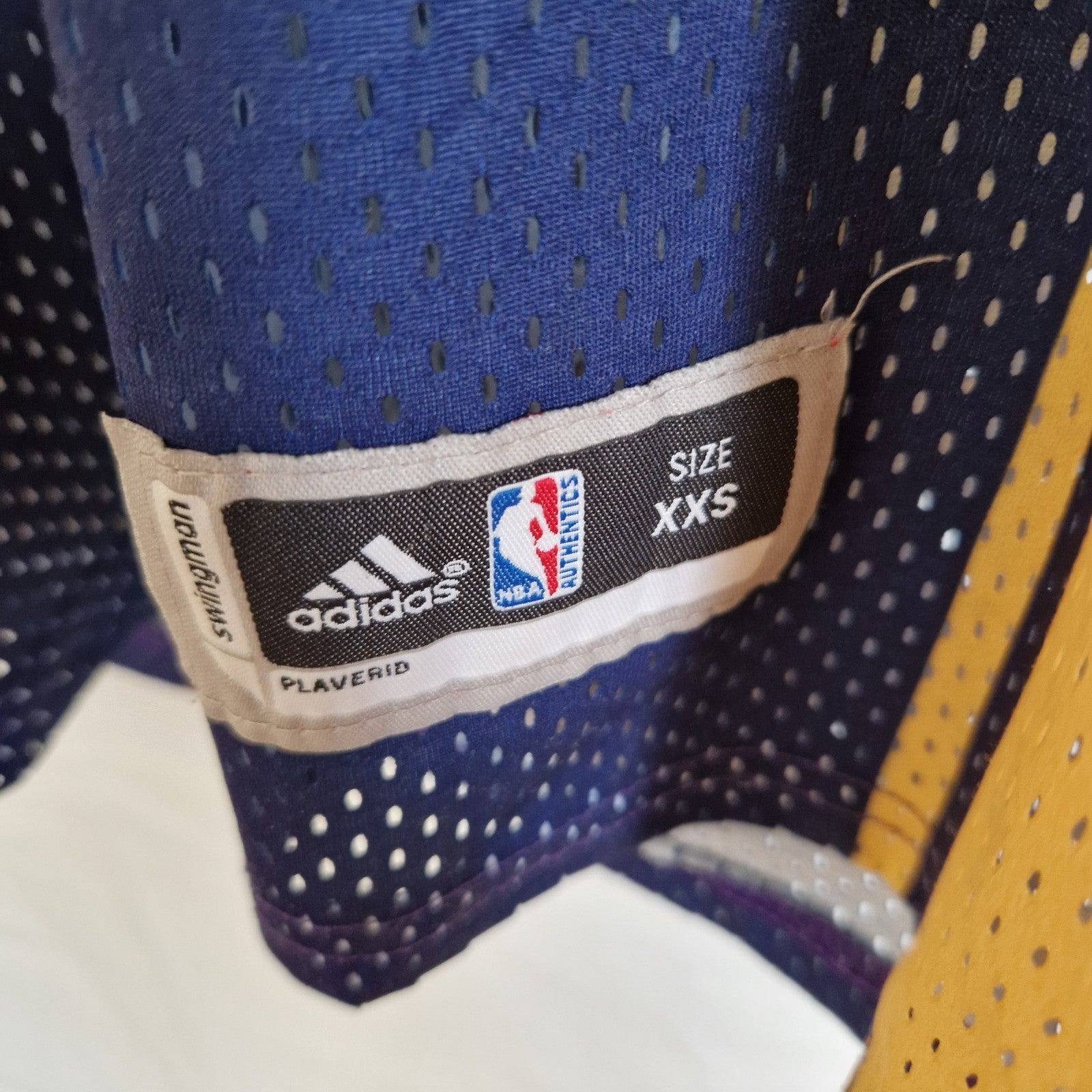 A close-up of an Adidas NBA Swingman jersey tag in size XXS on a blue mesh fabric.