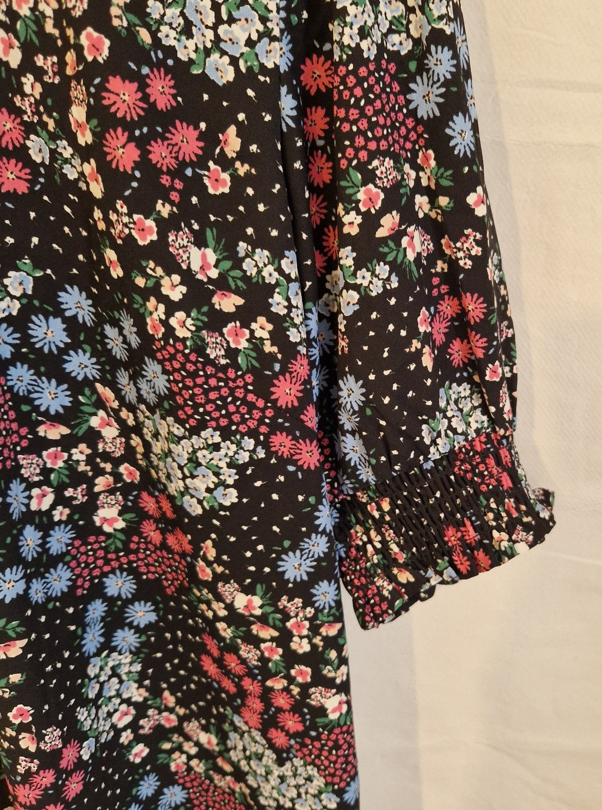A black short-sleeved blouse featuring a multicoloured floral print and a smocked cuff.