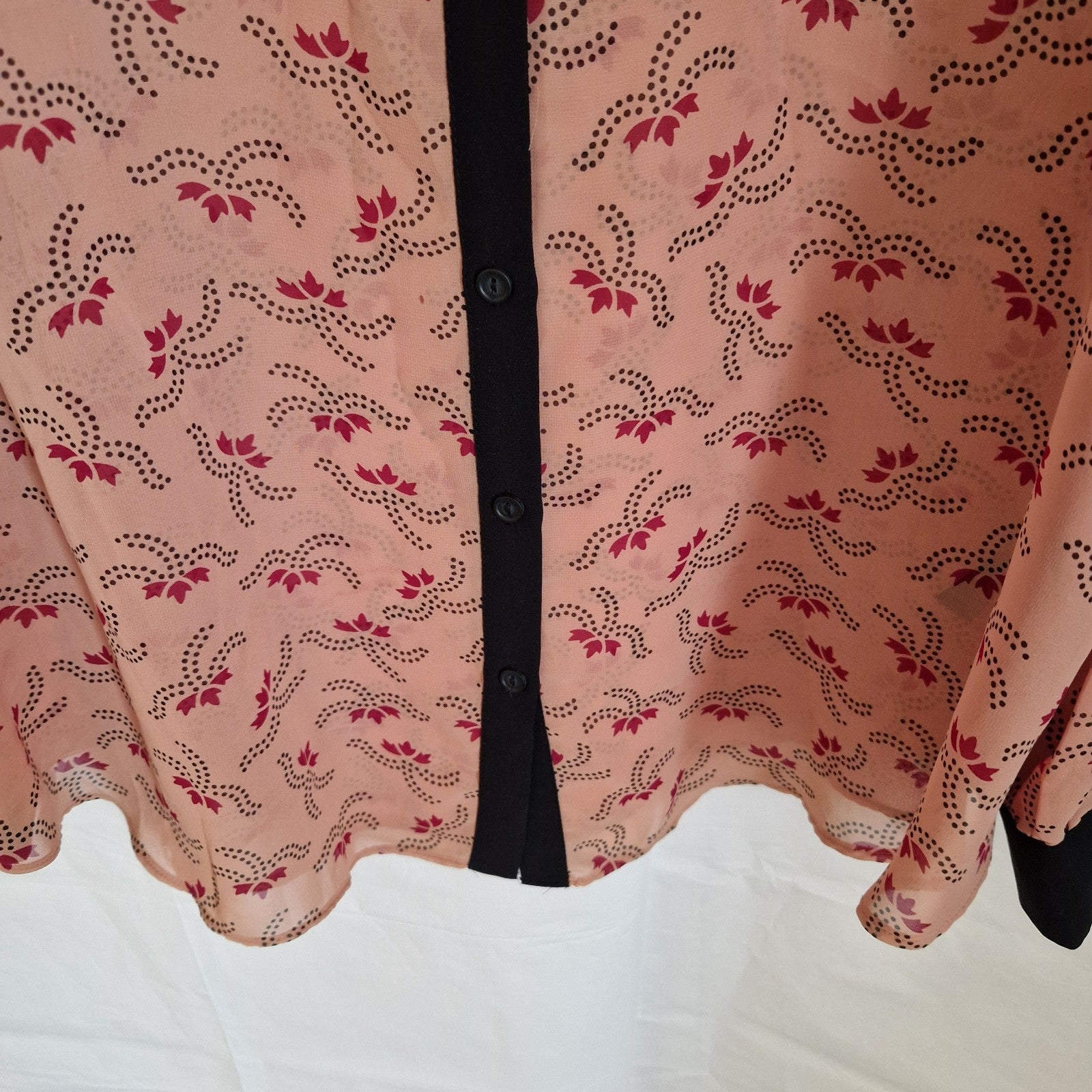 A peach-colored chiffon blouse with a black button placket and a repeating red floral pattern.