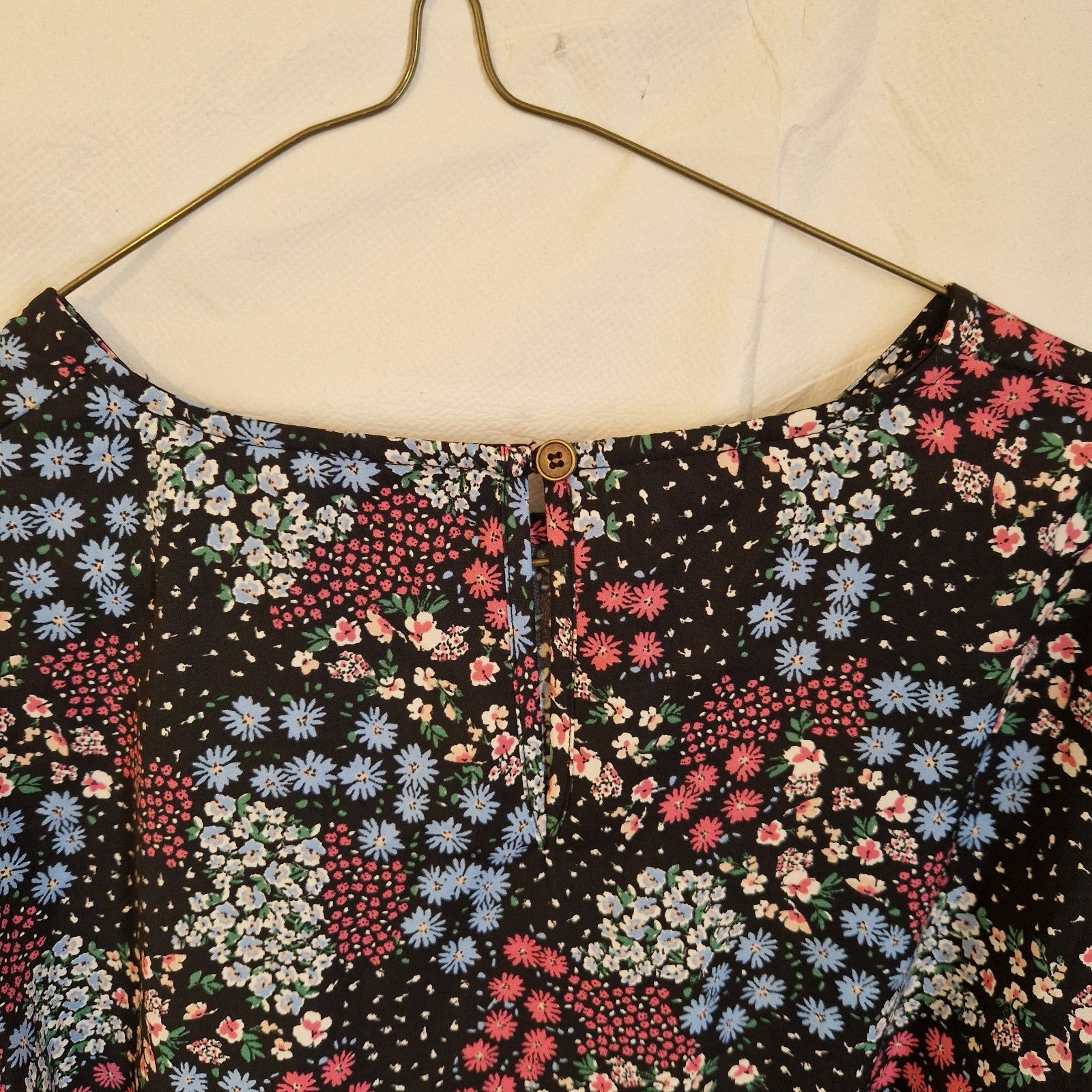 A black short-sleeved blouse featuring a multicoloured floral print and a button-back neckline.