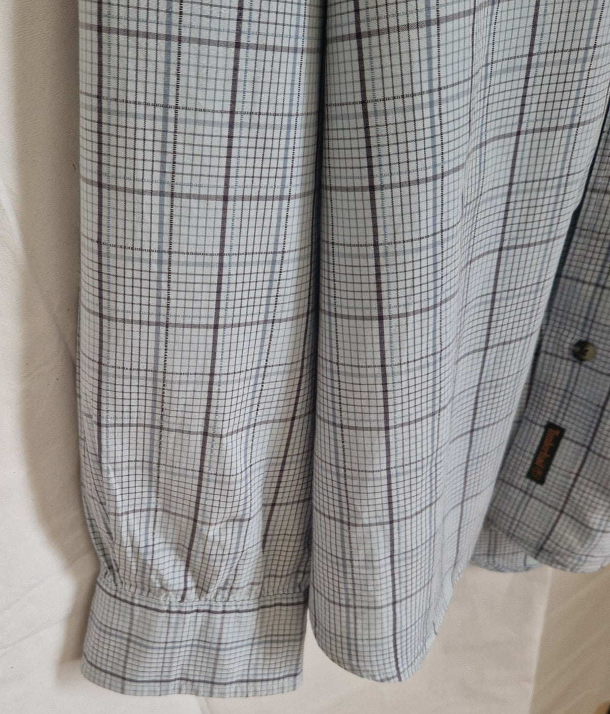 A long-sleeve Timberland shirt in a grey and blue check pattern with a buttoned cuff.