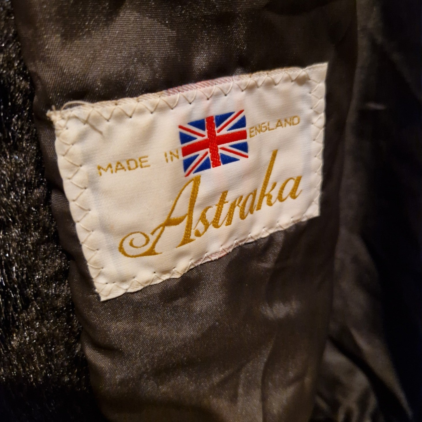 A close-up of a white Astraka brand label with a Union Jack flag sewn into a dark brown faux fur coat.