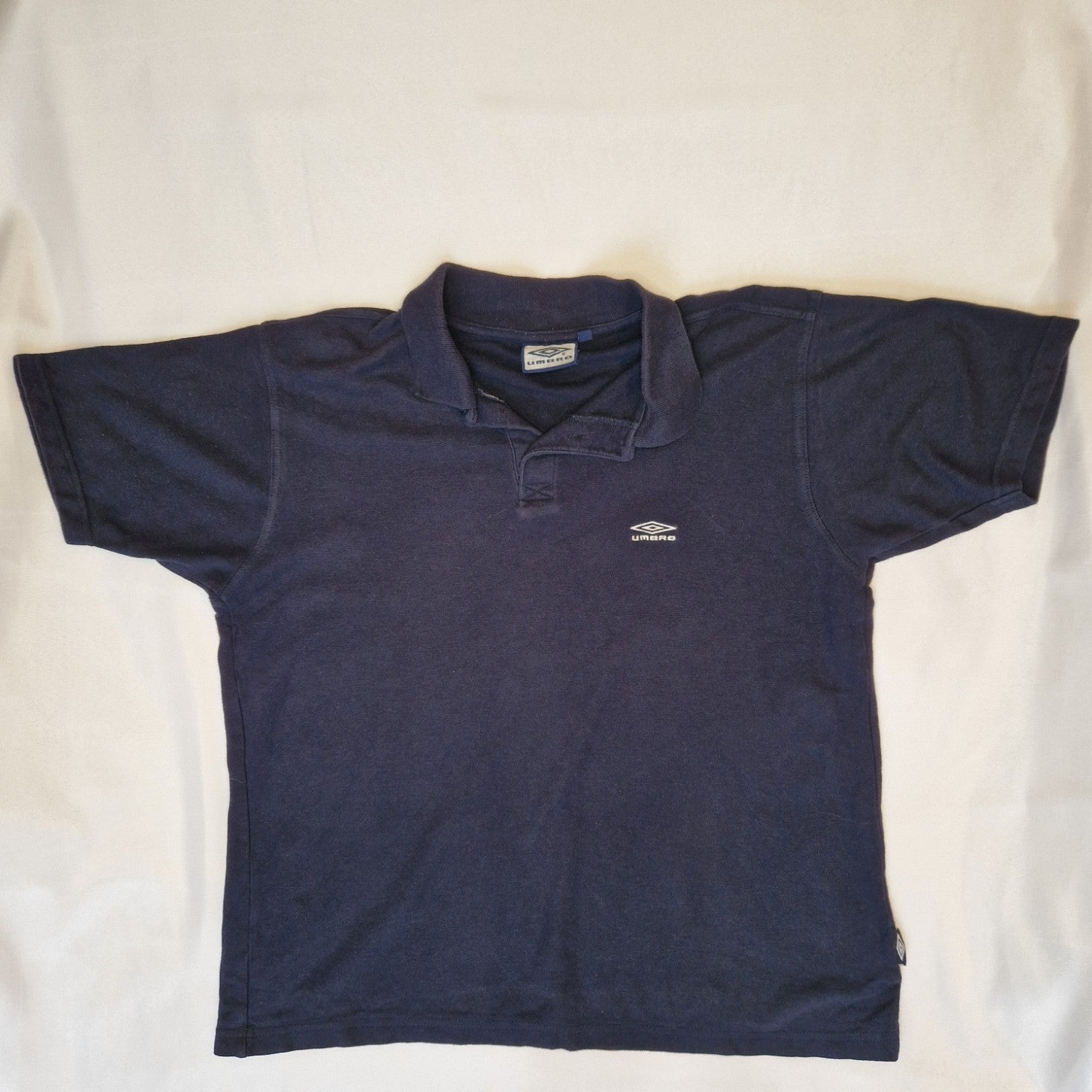 A navy blue Umbro short-sleeve polo shirt made of cotton jersey with a button-up collar.