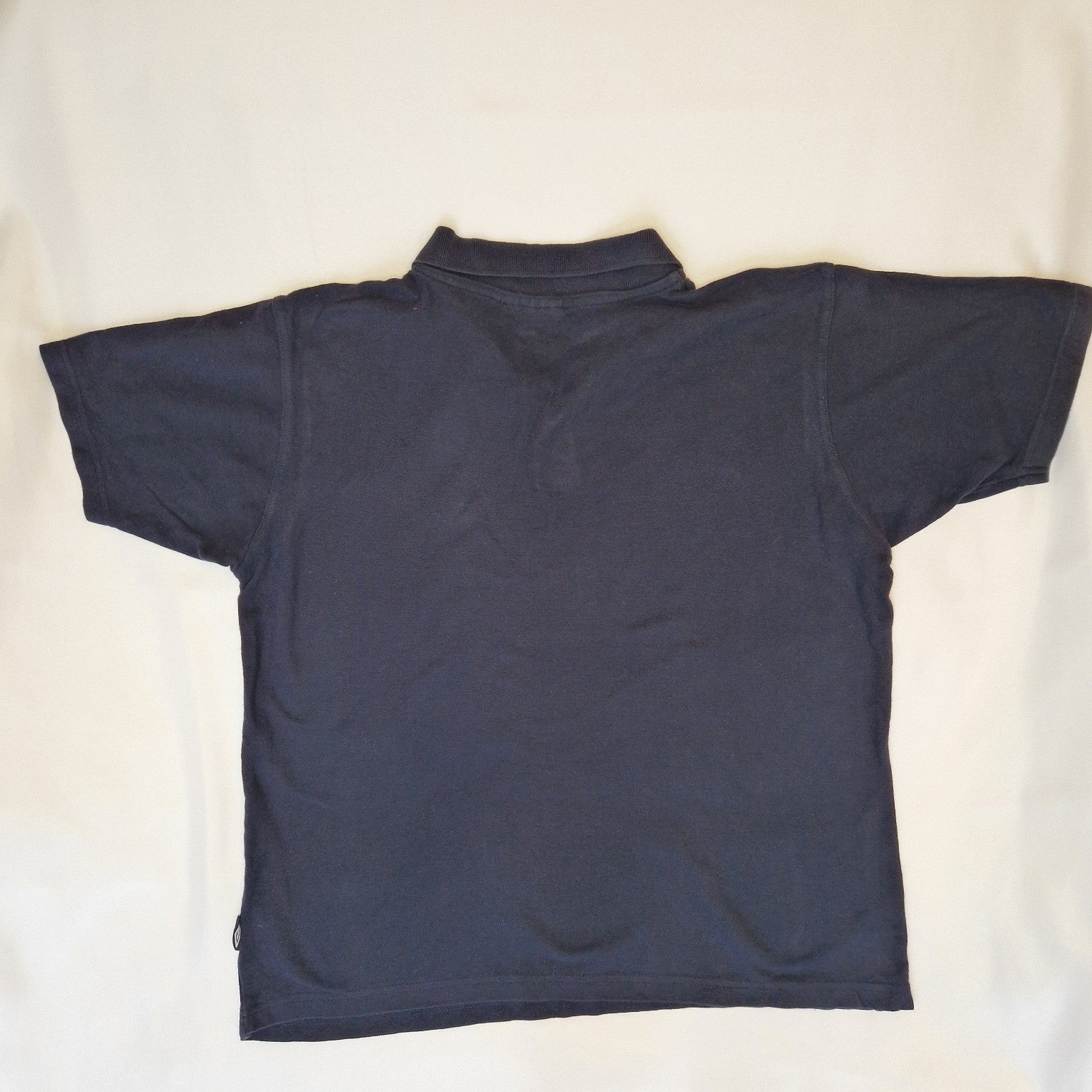 A navy blue Umbro short sleeve polo shirt made from cotton jersey with a point collar.
