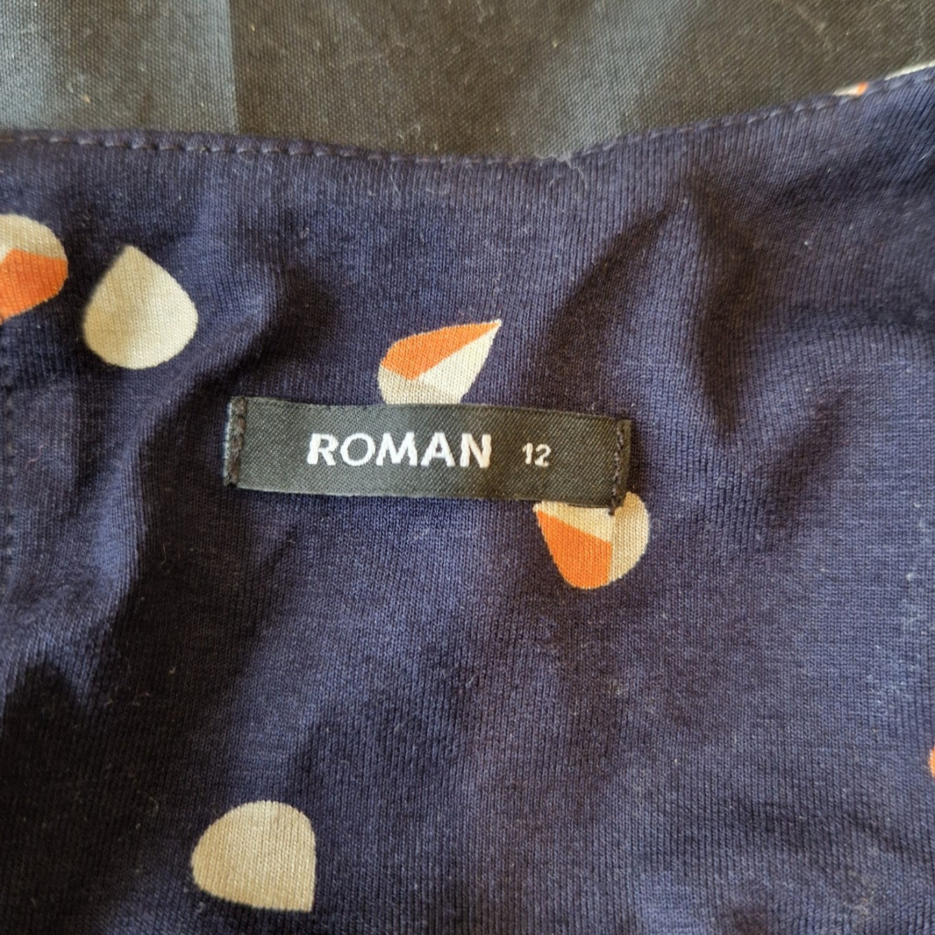 A close-up of a navy blue Roman brand dress label in size 12 with a multicoloured floral print.