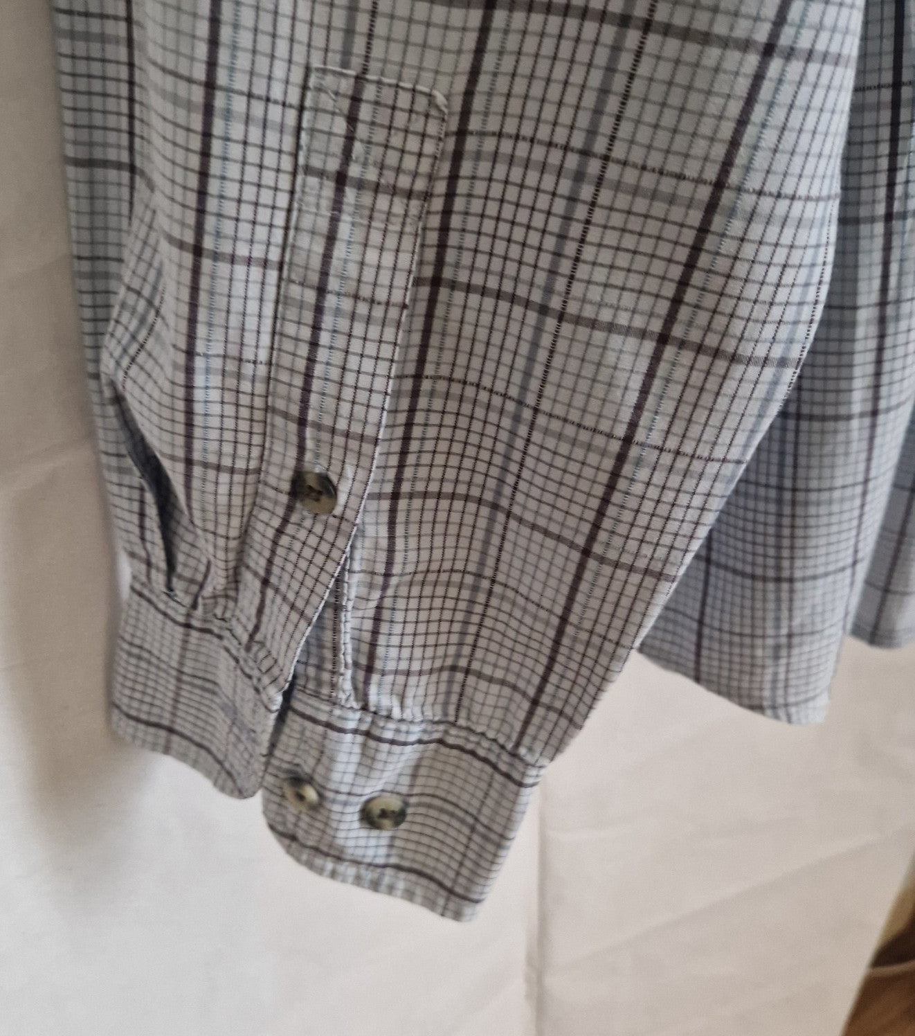 A close-up of a grey and blue check long-sleeve shirt cuff with button closures.