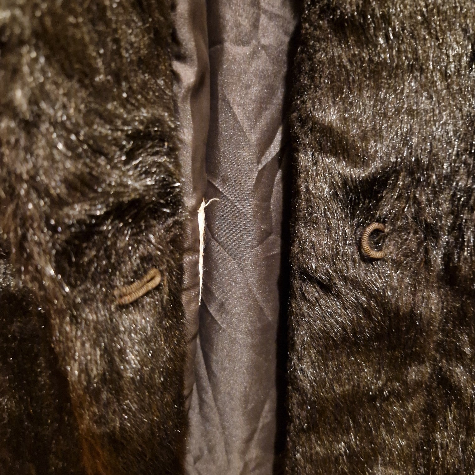 A close-up of a dark brown Astraka faux fur coat showing the hook and eye closure.