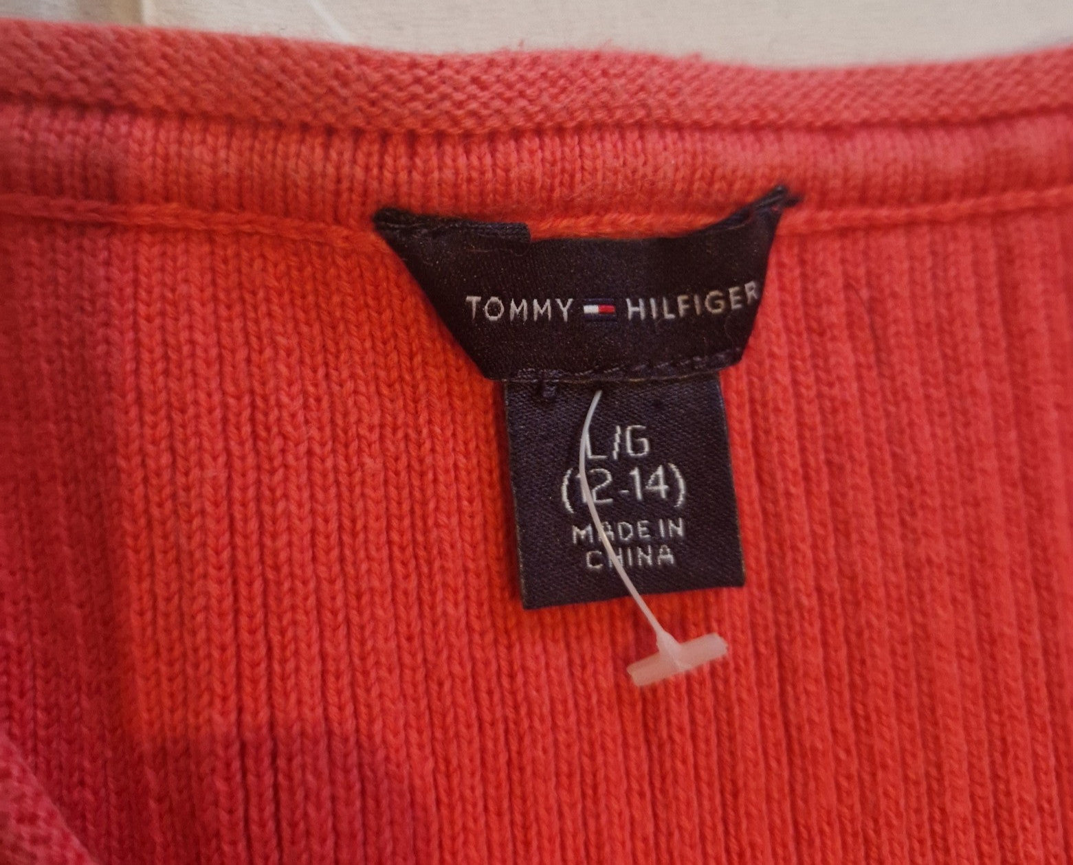A close-up of a red Tommy Hilfiger jumper dress label showing size L 12-14 made in China.