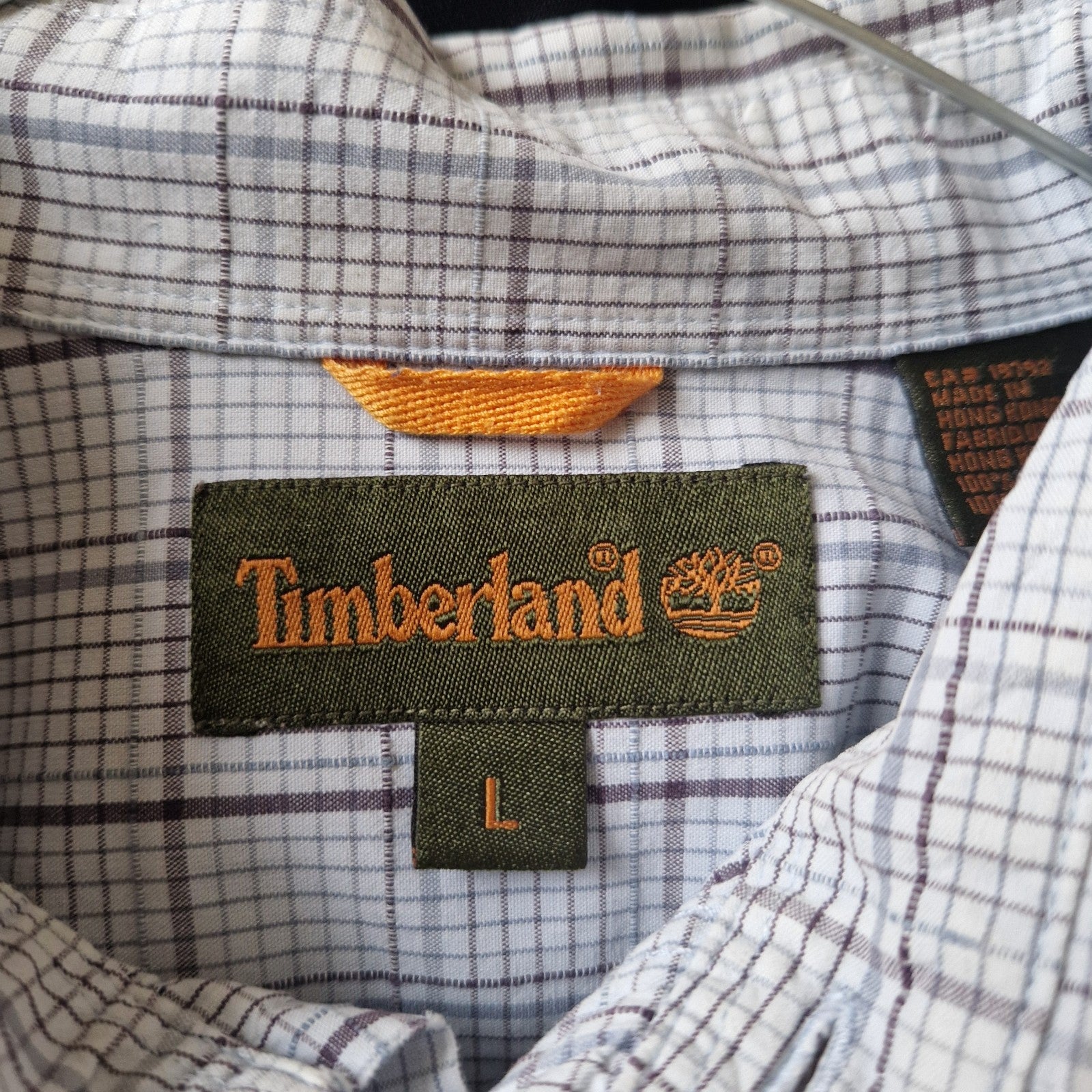 A close-up of the interior collar label on a grey and blue check Timberland long-sleeve shirt.