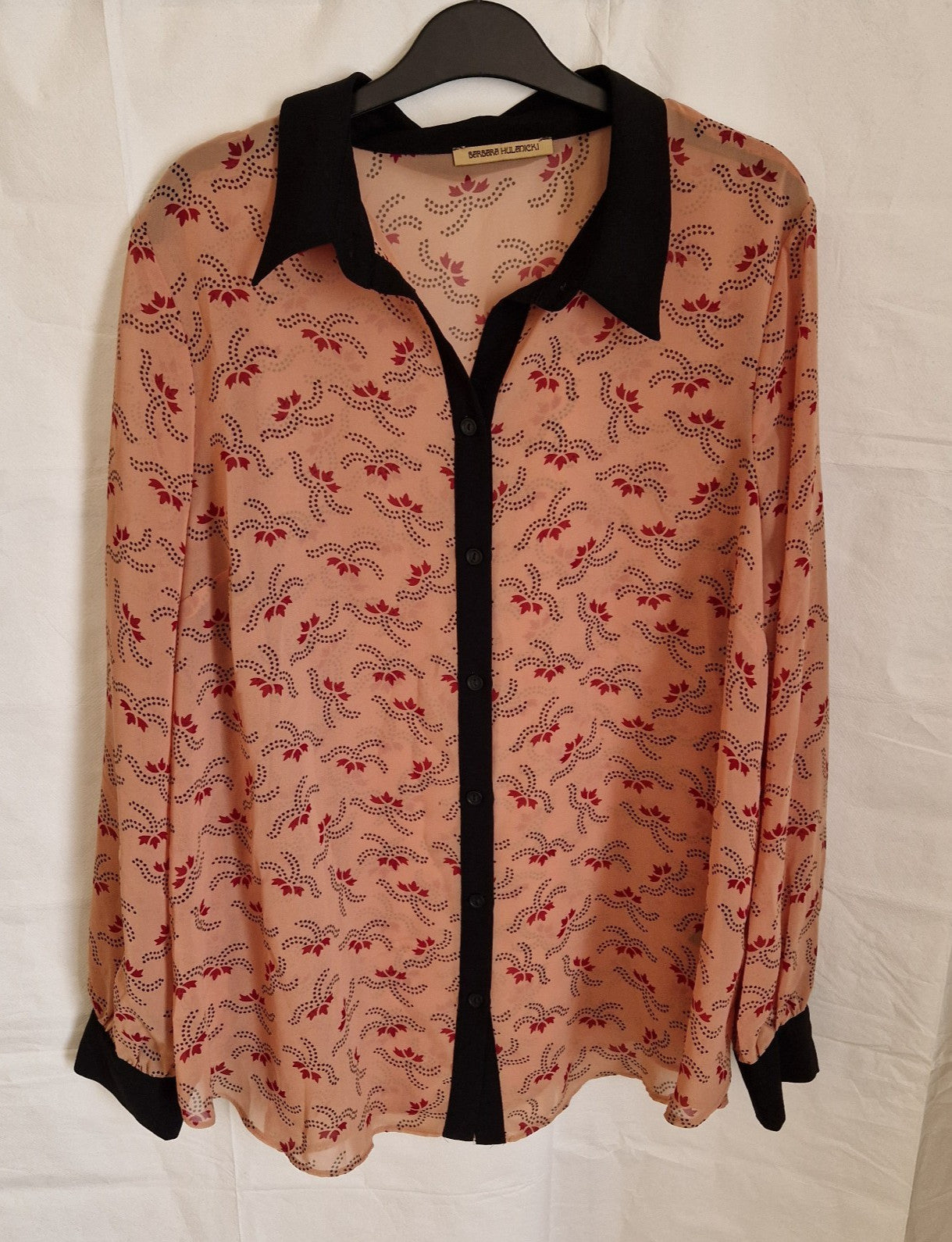 A long-sleeved, button-up chiffon blouse in peach with a black collar, cuffs, and placket.