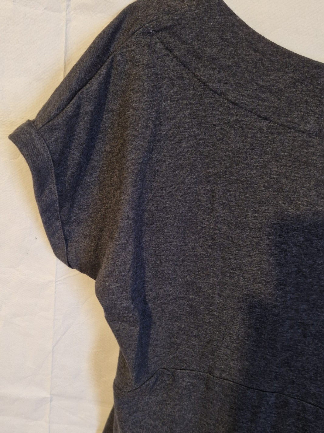 A close-up of a grey cotton blend jersey shift dress featuring a round neckline and cuffed sleeves.