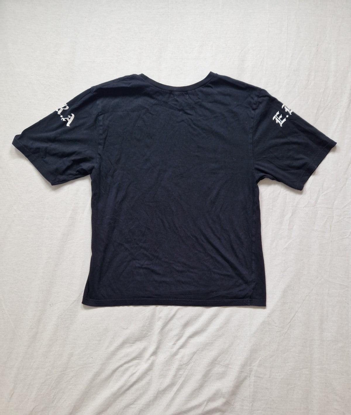 Black t-shirt with white text on sleeves laid flat on a light-colored surface