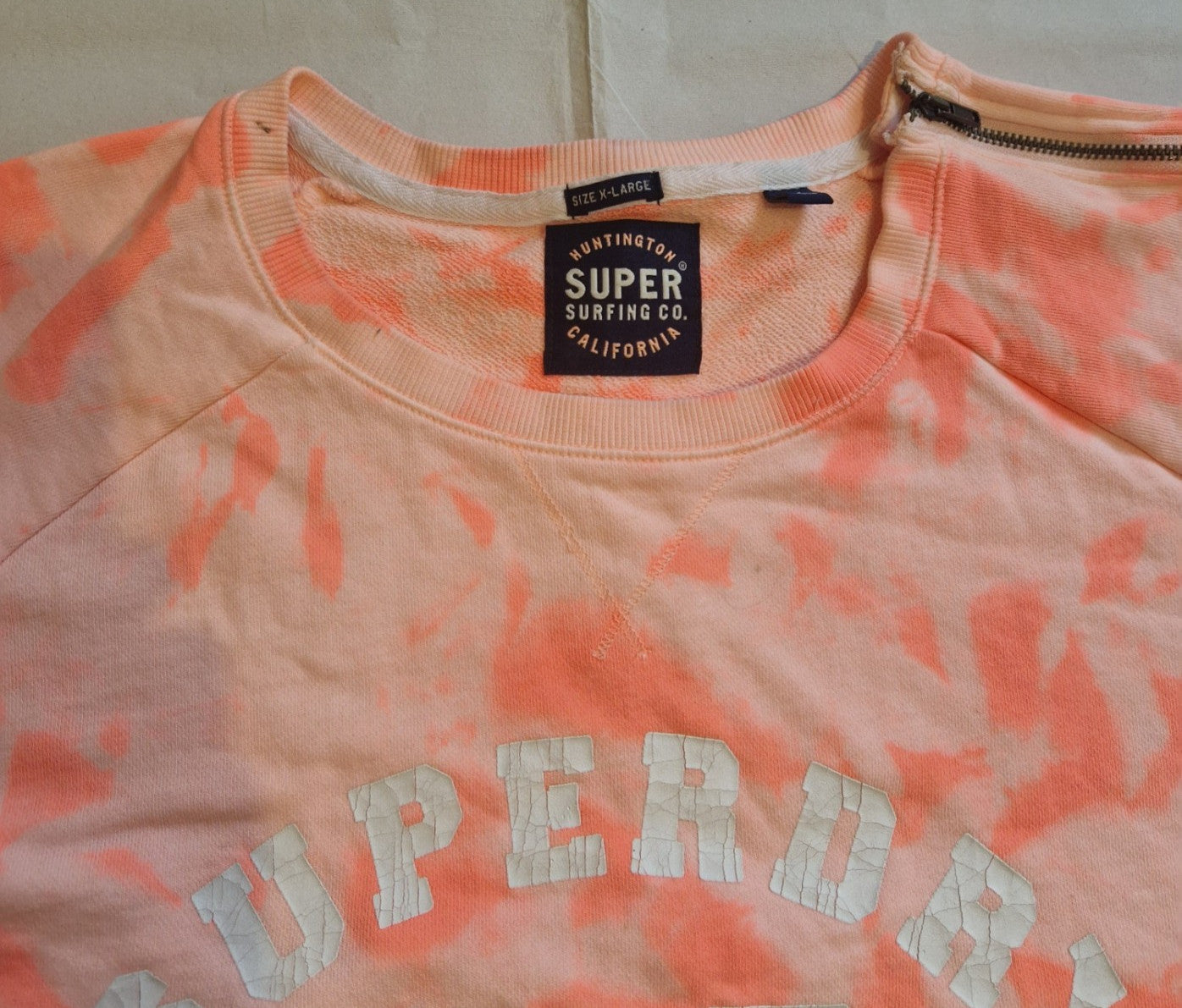 A pink and orange tie-dye Superdry quarter-zip sweatshirt with a cracked graphic logo.