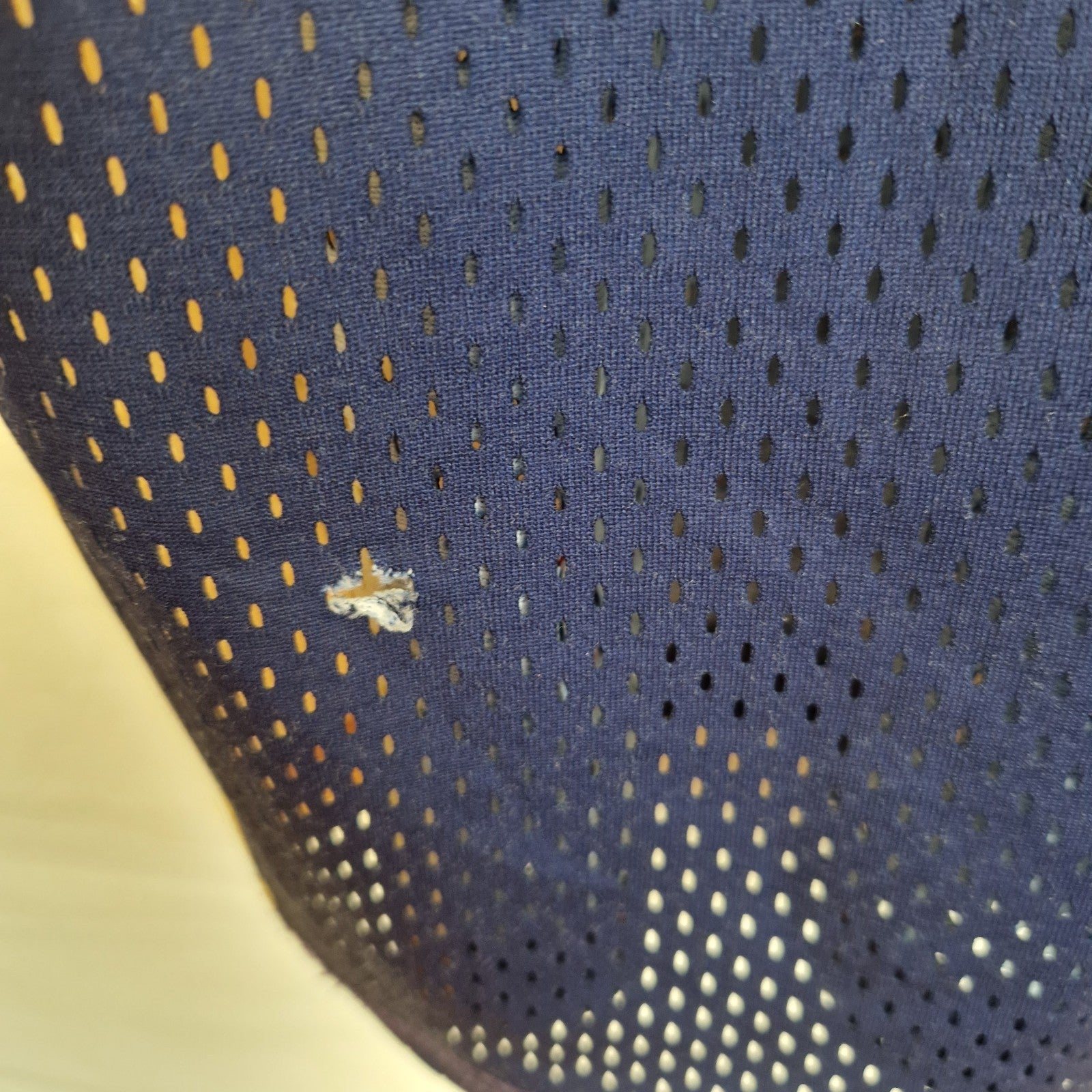A close-up view of a navy blue mesh basketball jersey showing a small snag in the fabric.
