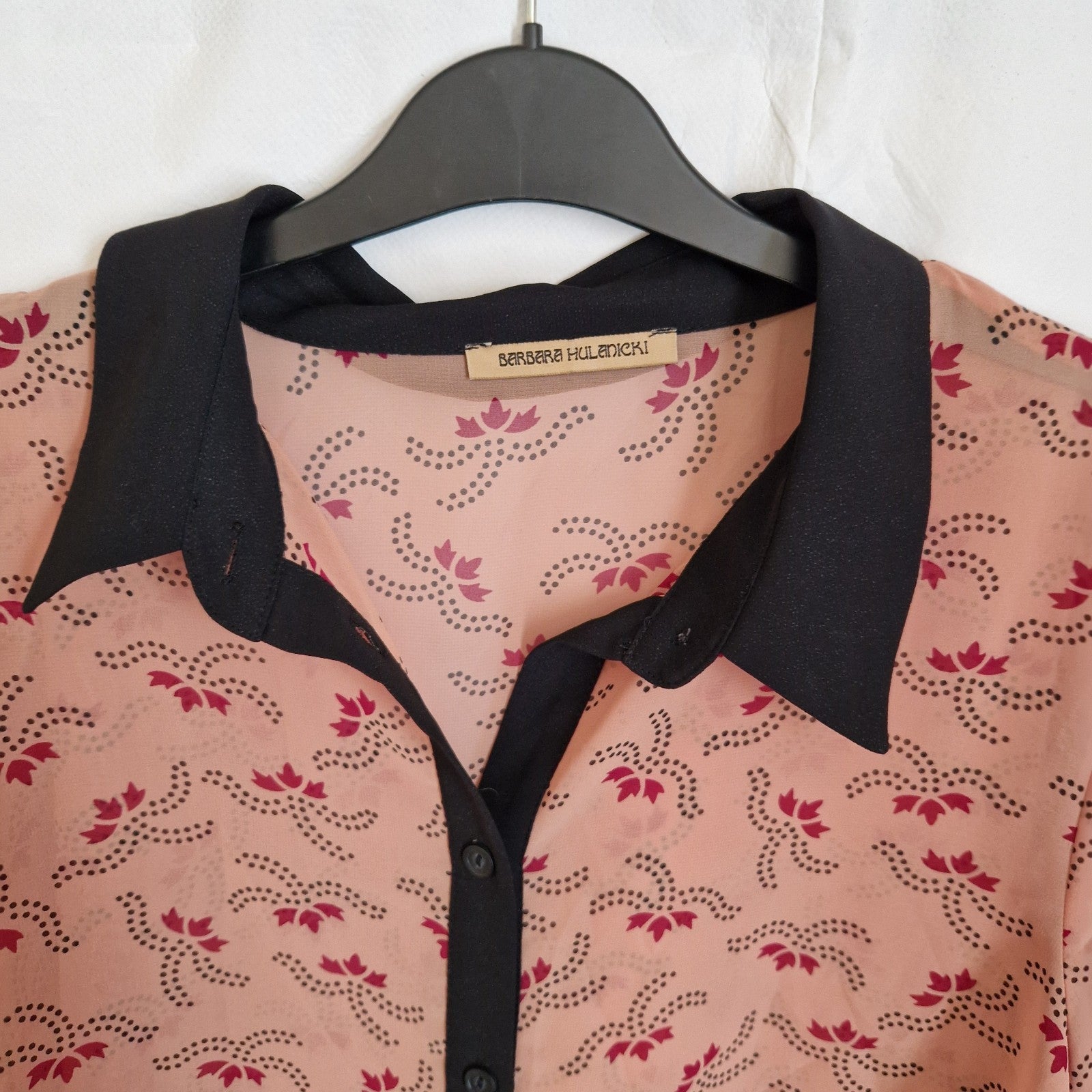 A peach-colored chiffon blouse by Barbara Hulanicki featuring a black collar, button-front, and a repeating dark pink floral pattern.