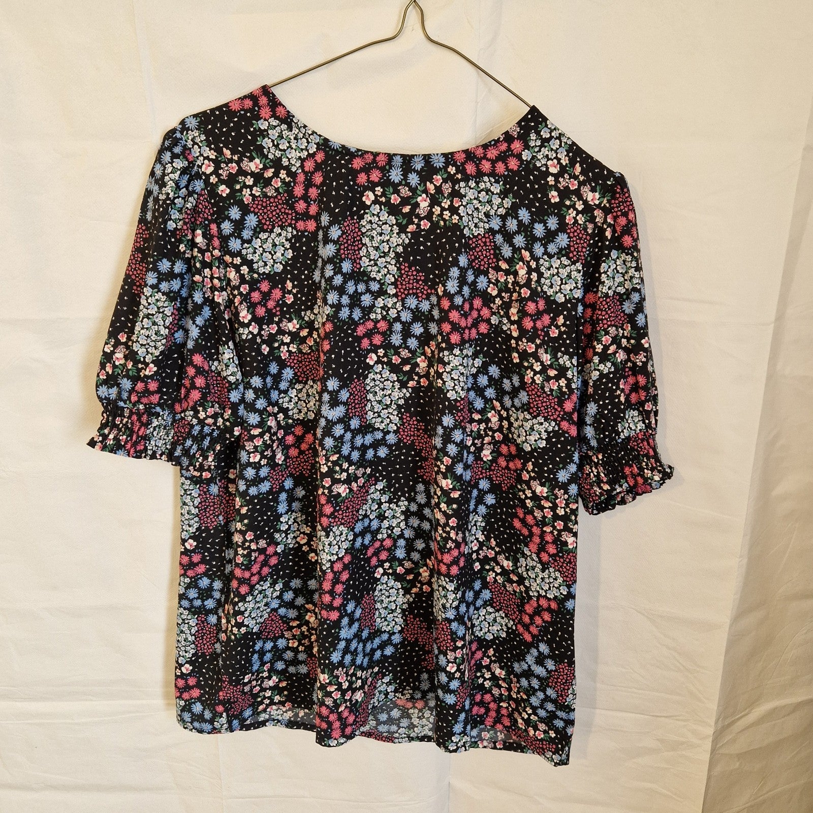 A black short-sleeve blouse with a multicoloured floral print and a round neckline.