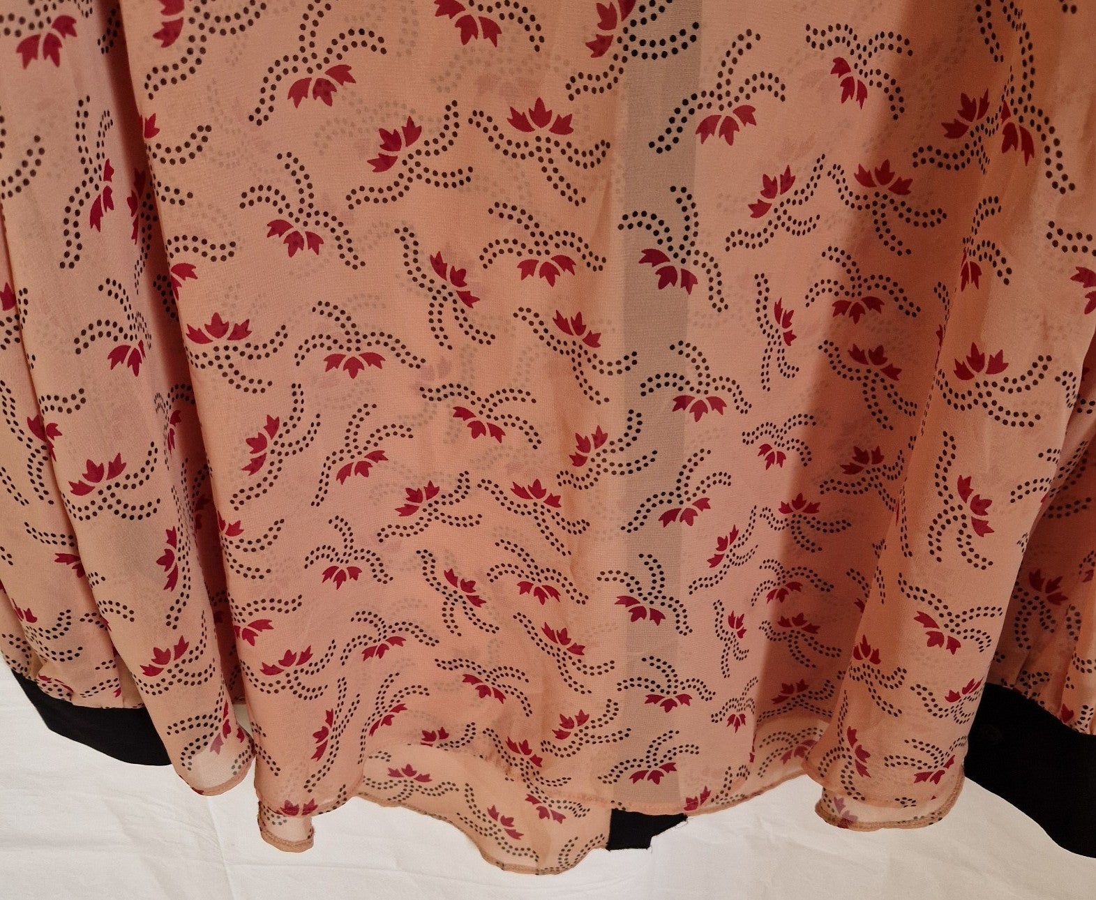 A peach-colored chiffon blouse featuring a repeating dark red floral pattern and black cuffs.