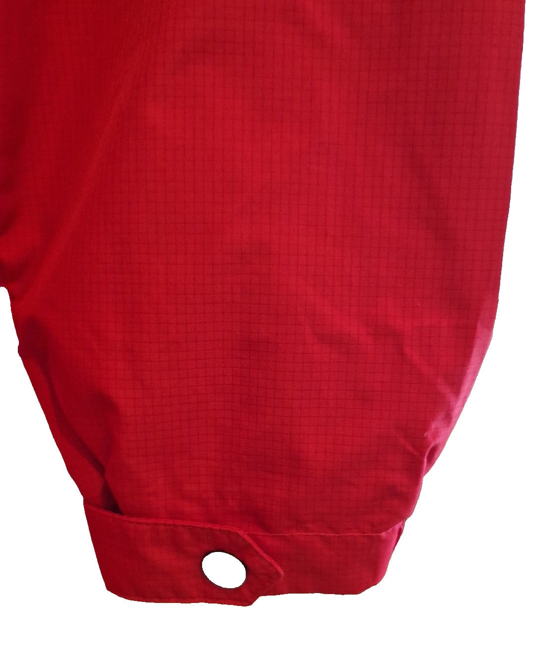 A close-up of a red, grid-patterned polyester sleeve with a buttoned cuff on a training jacket.