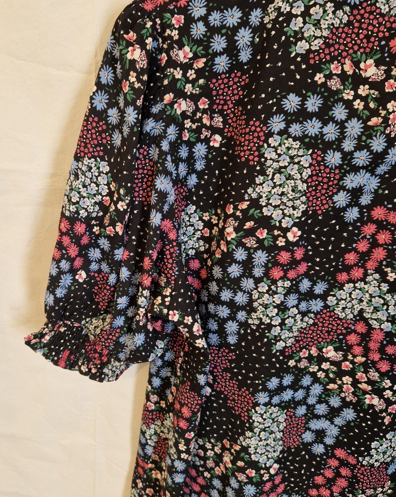 A black short-sleeve blouse featuring a vibrant multicoloured floral print and ruffled cuffs.